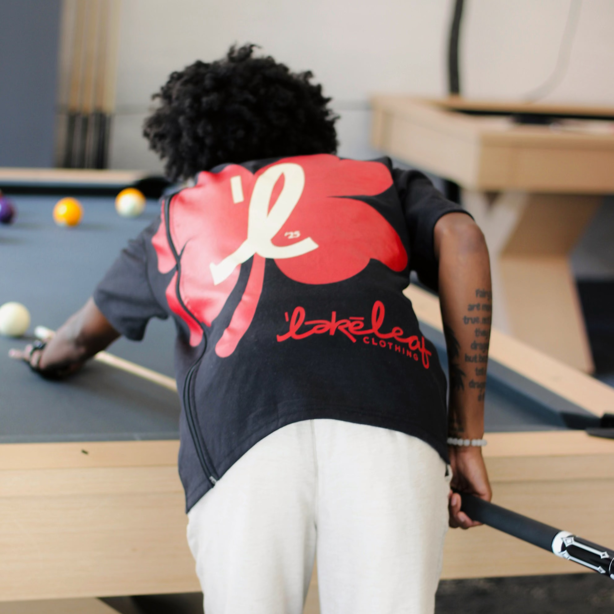 Leaf playing pool wearing a black t-shirt with red and white designs.